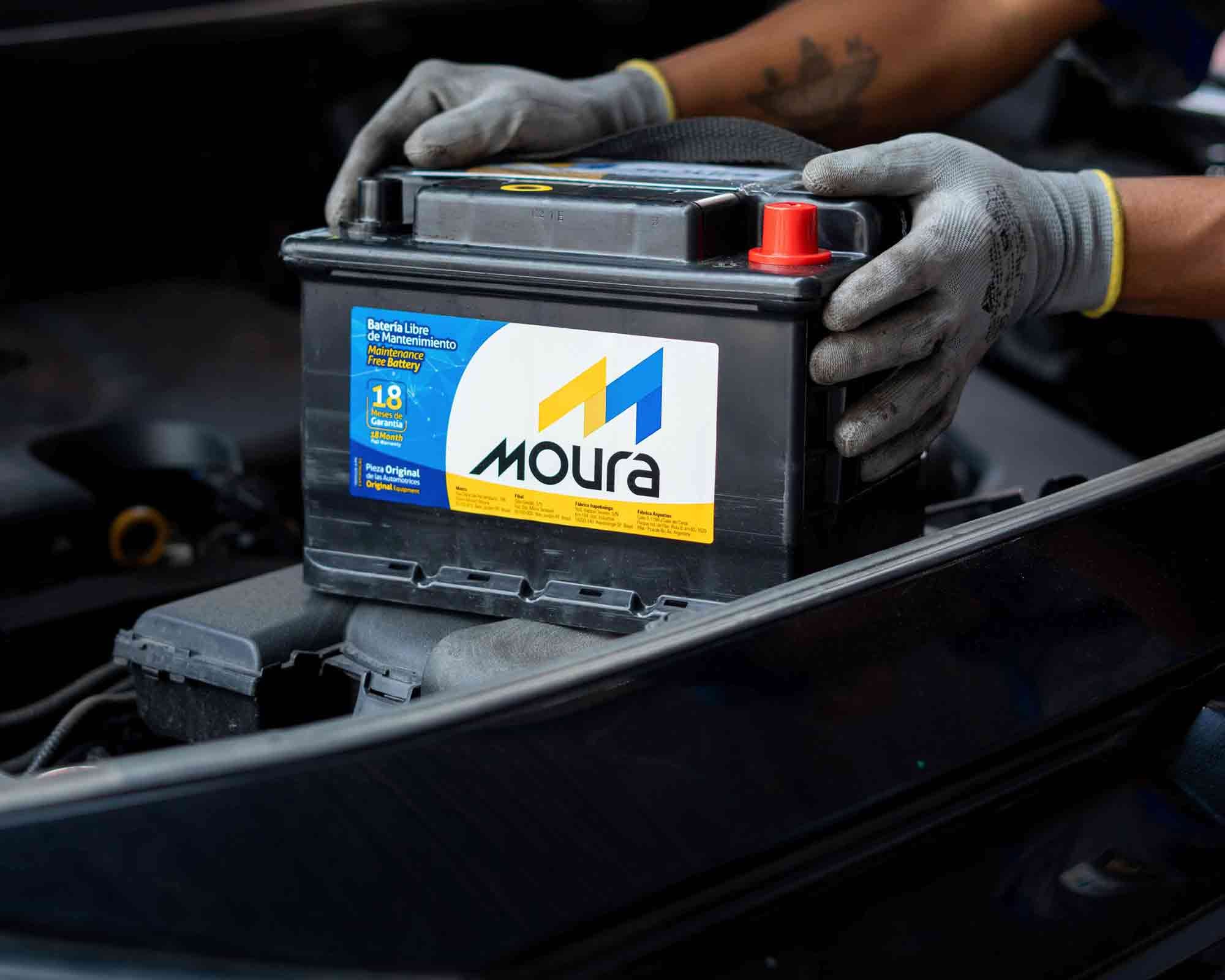 Hombre con una batería Moura de automóvil en la mano, listo para realizar una tarea mecánica.