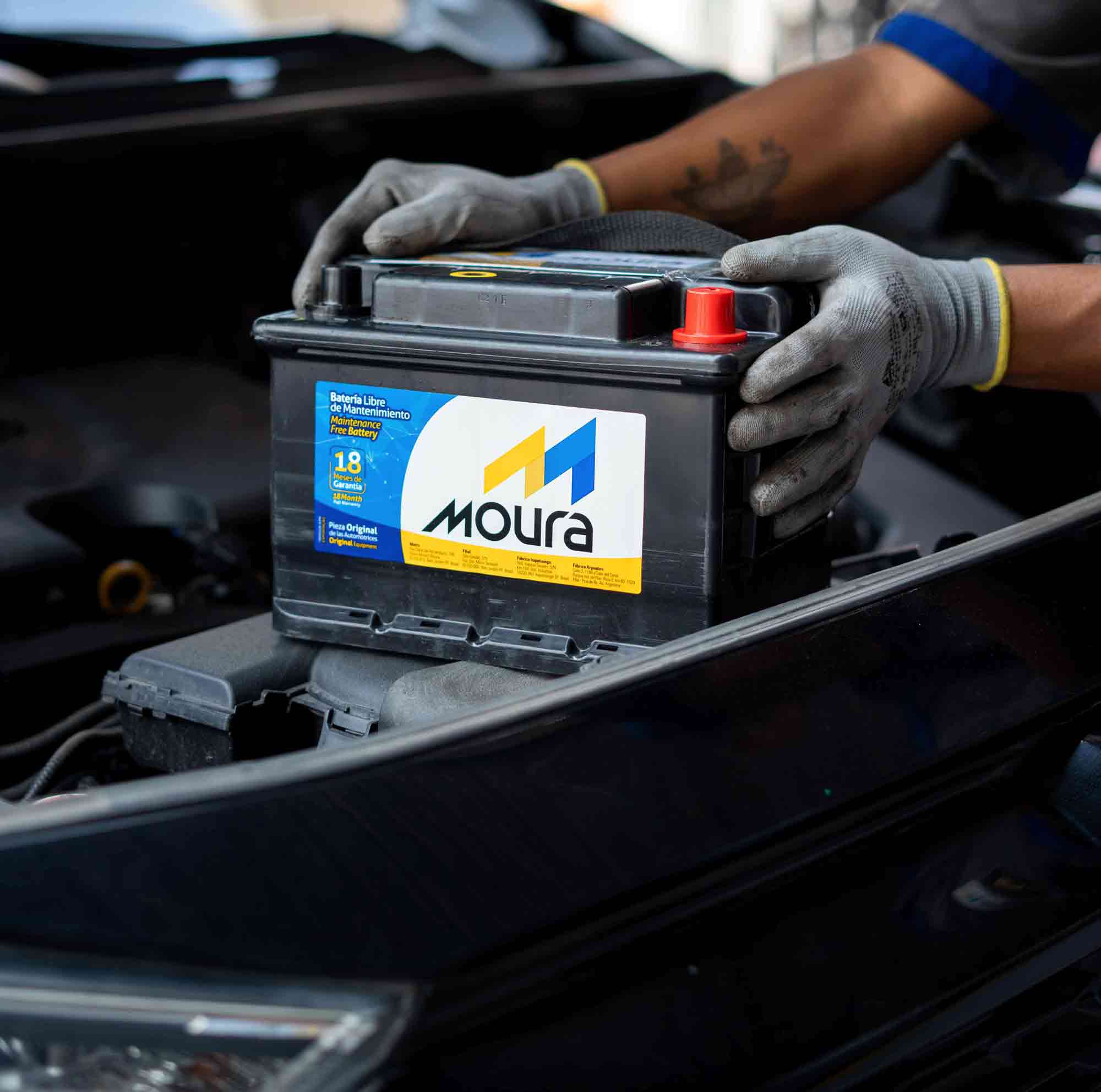 Hombre con una batería Moura de automóvil en la mano, listo para realizar una tarea mecánica.
