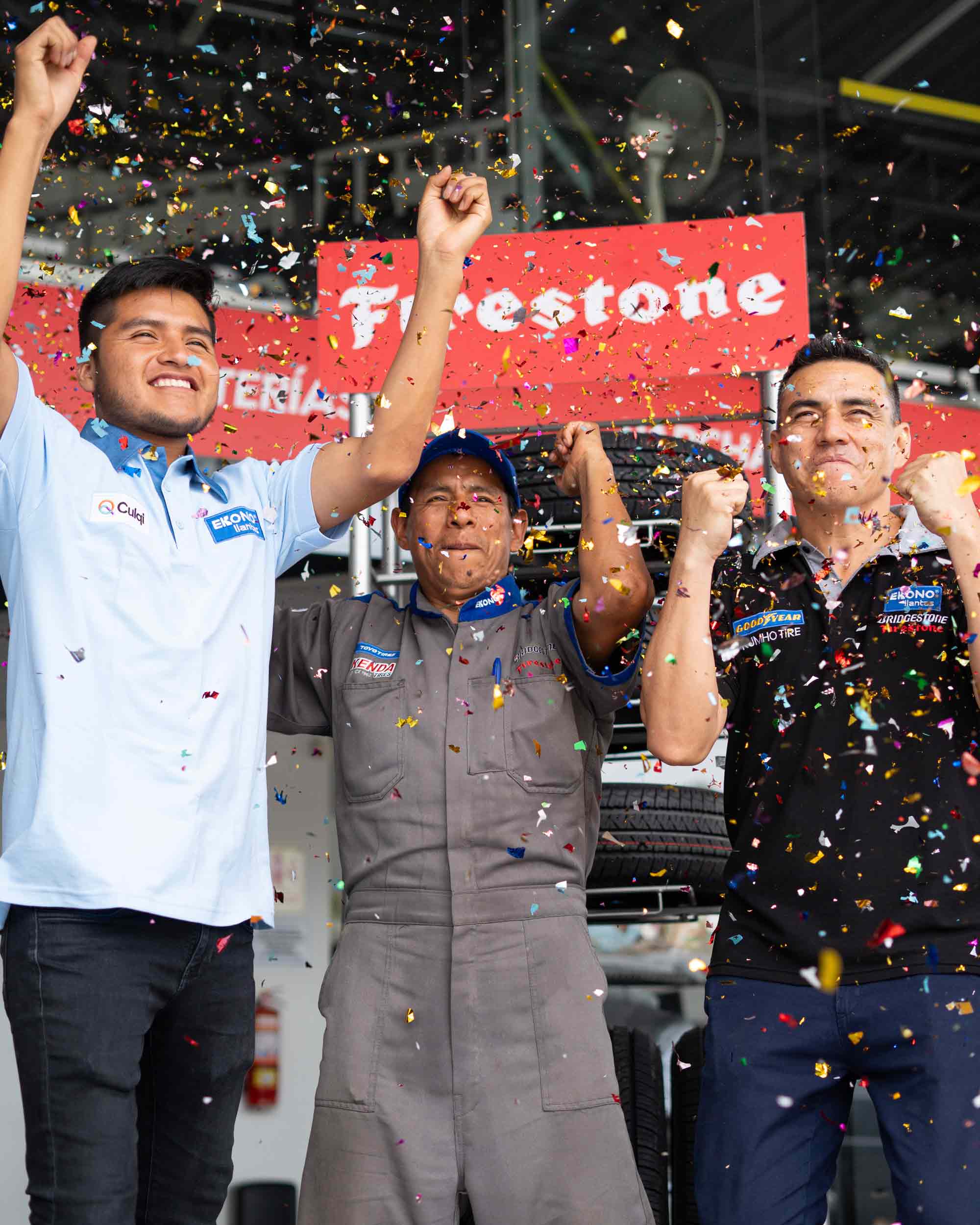Tres hombres con uniforme de ekono llantas y pantalones negros sosteniendo un cartel de Firestone.